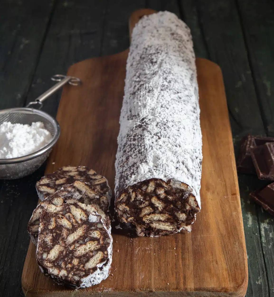 Chocolate salami with 3 slices cut on a wooden board.