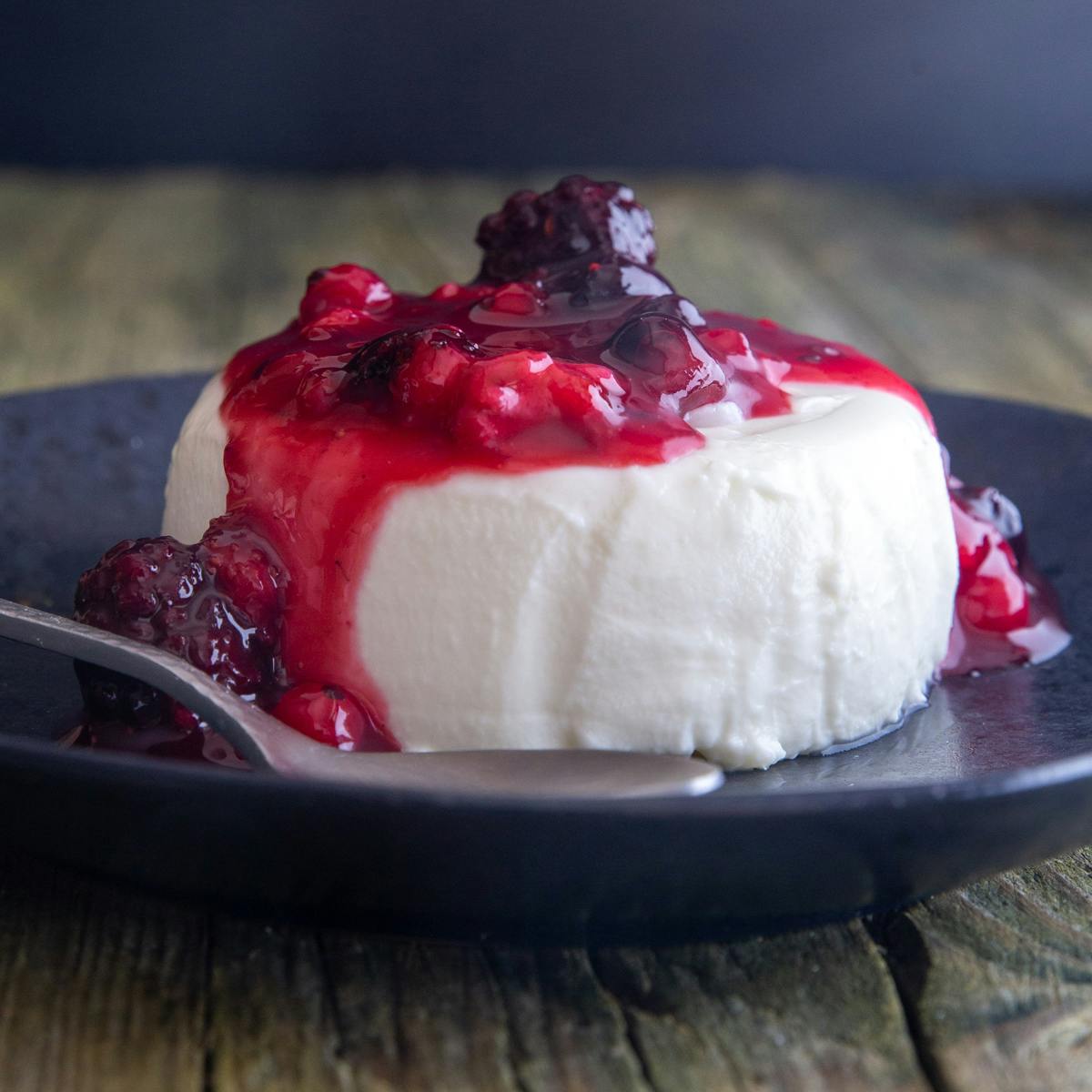 Panna cotta on a black plate with a silver spoon.