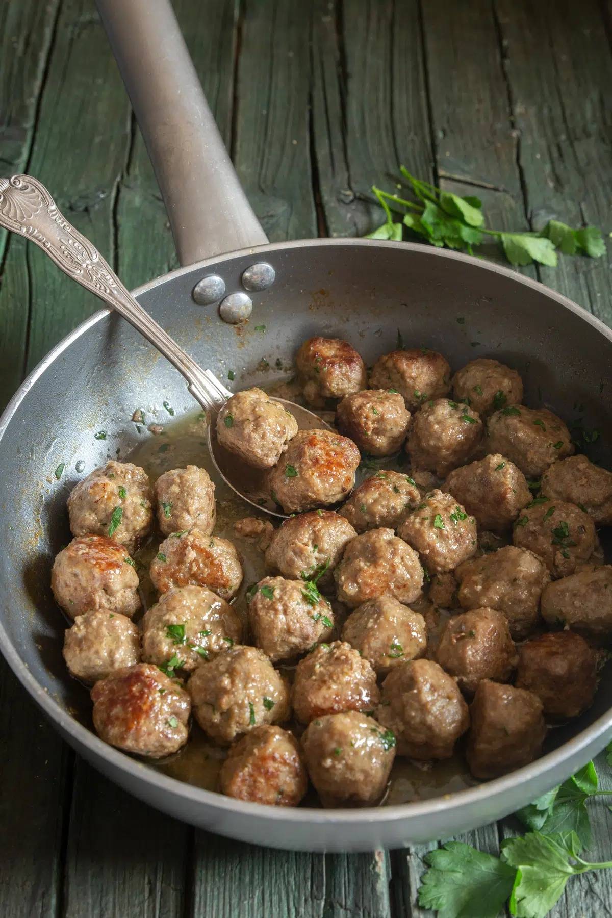 Italian meatballs in a pan with two on a sppon.
