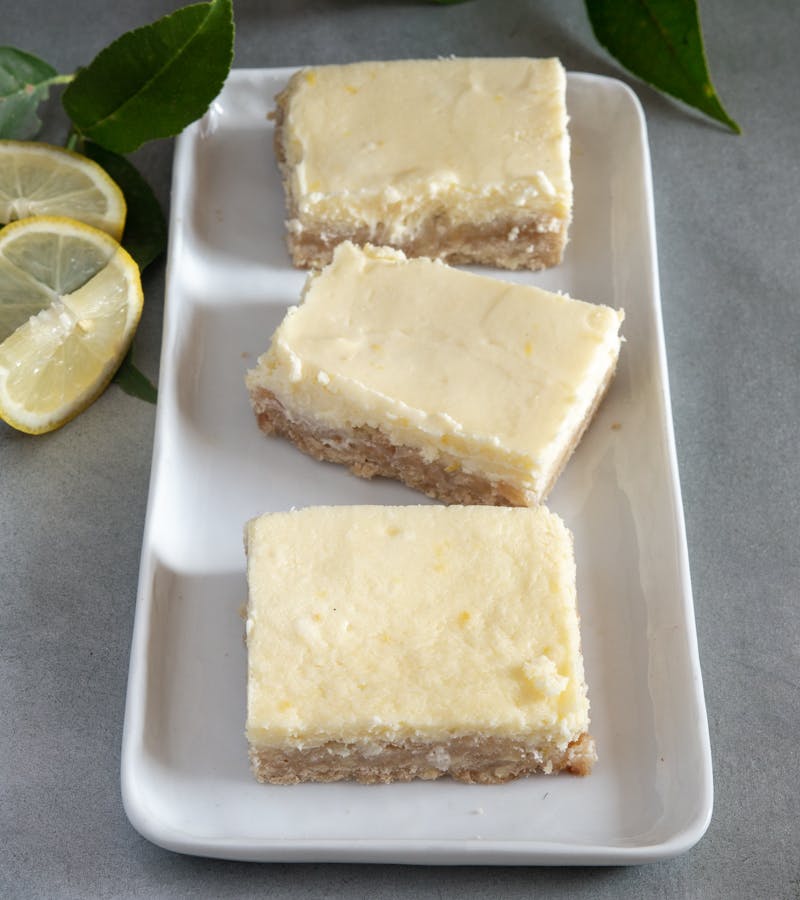 3 lemon cheesecake squares on a white plate.