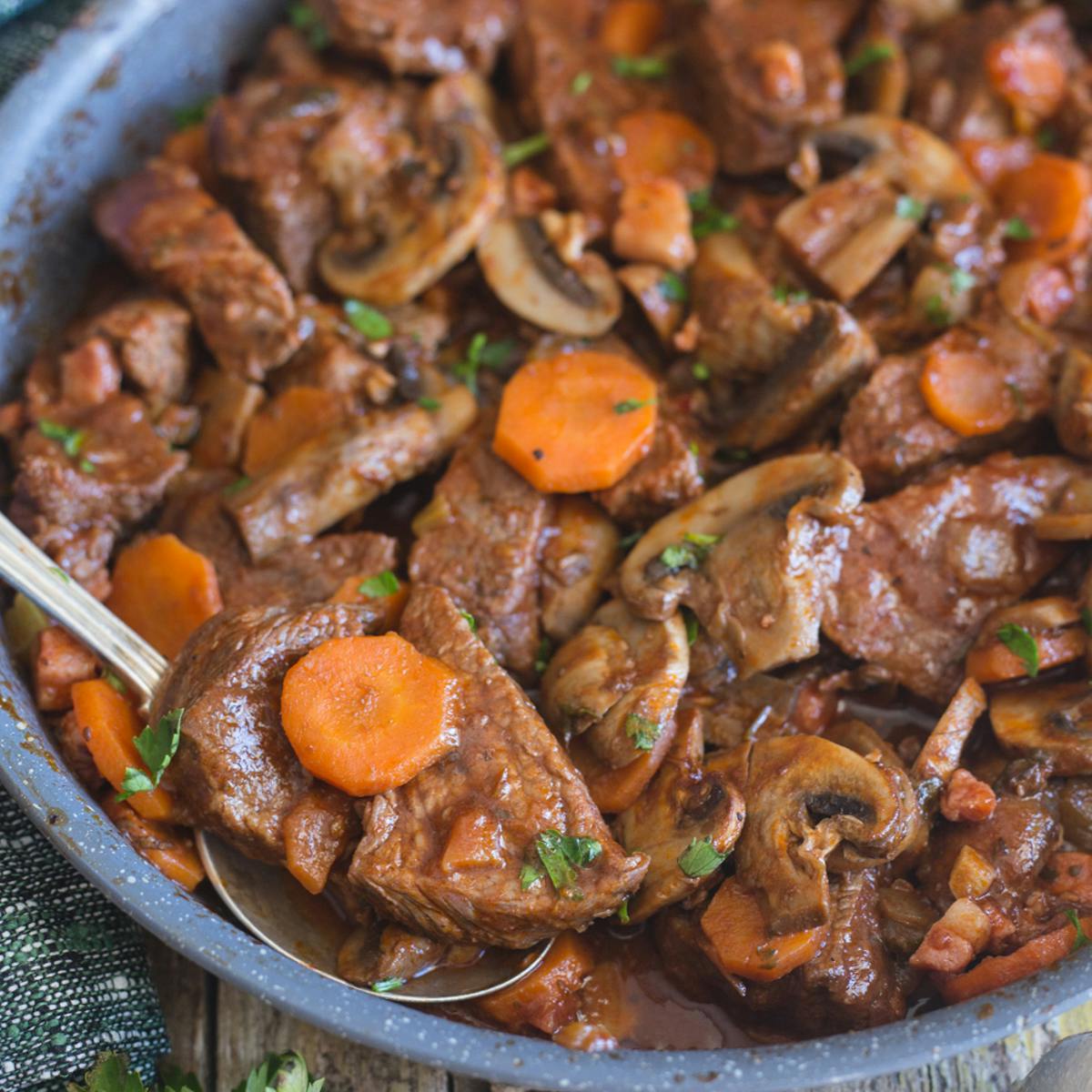 Beef stew in a frying pan with a silver spoon.