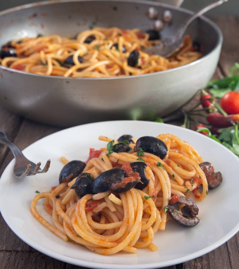 Pasta puttanesca in a pan and on a white plate.