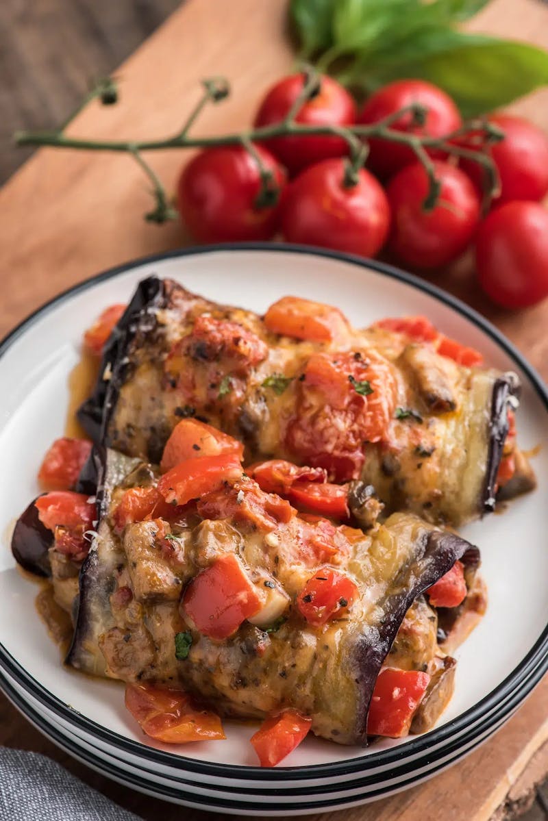 Two vegetable stuffed eggplant rolls on a white plate.