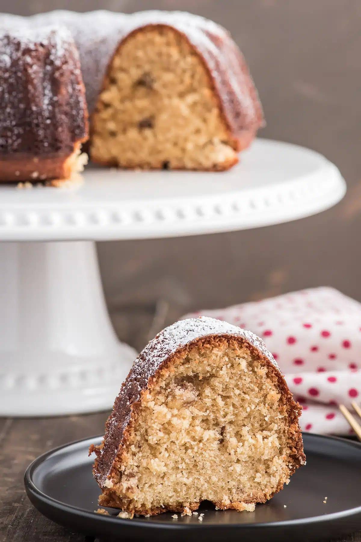 Bundt cake on a white cake plate with a slice on a black plate.