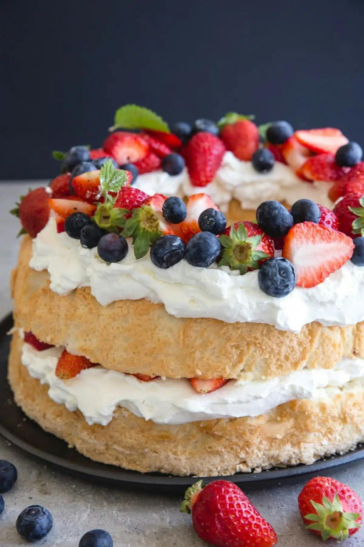 Homemade angel food cake with berries on a black plate.