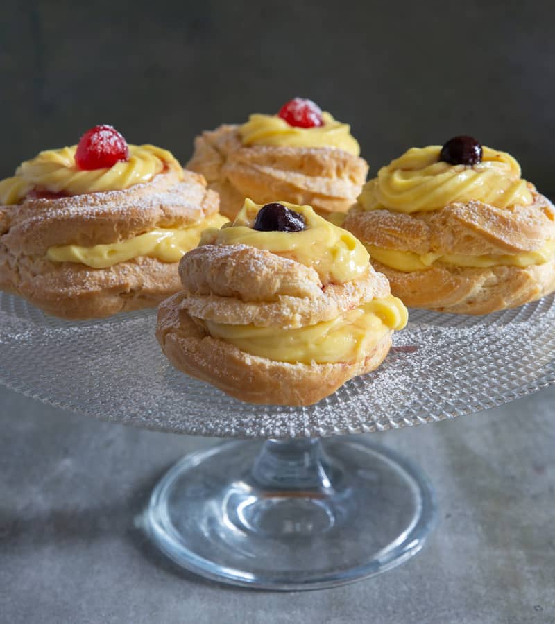 Four zeppole on a glass cake stand.