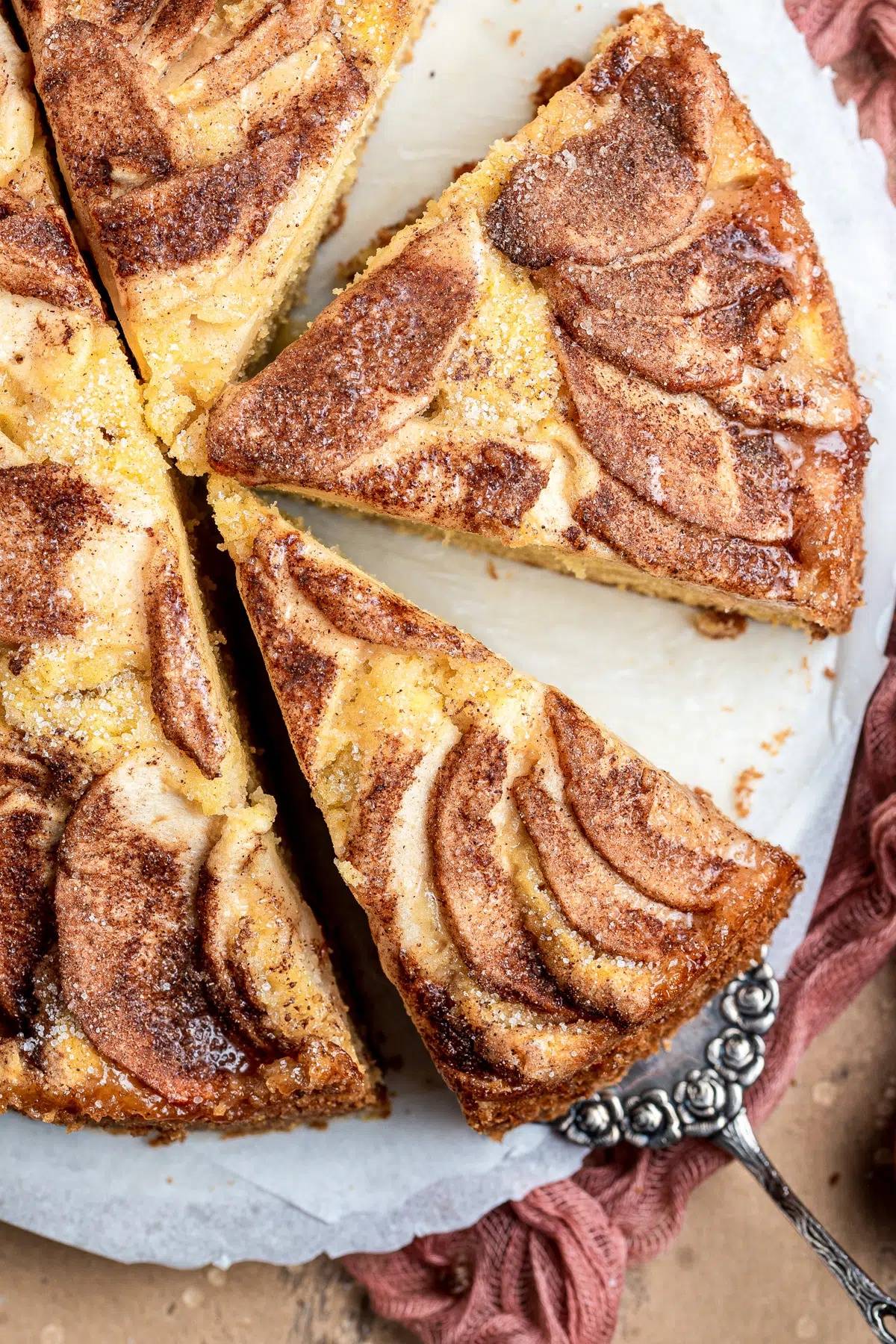 Apple cinnamon cake on a white plate with 2 slices cut.