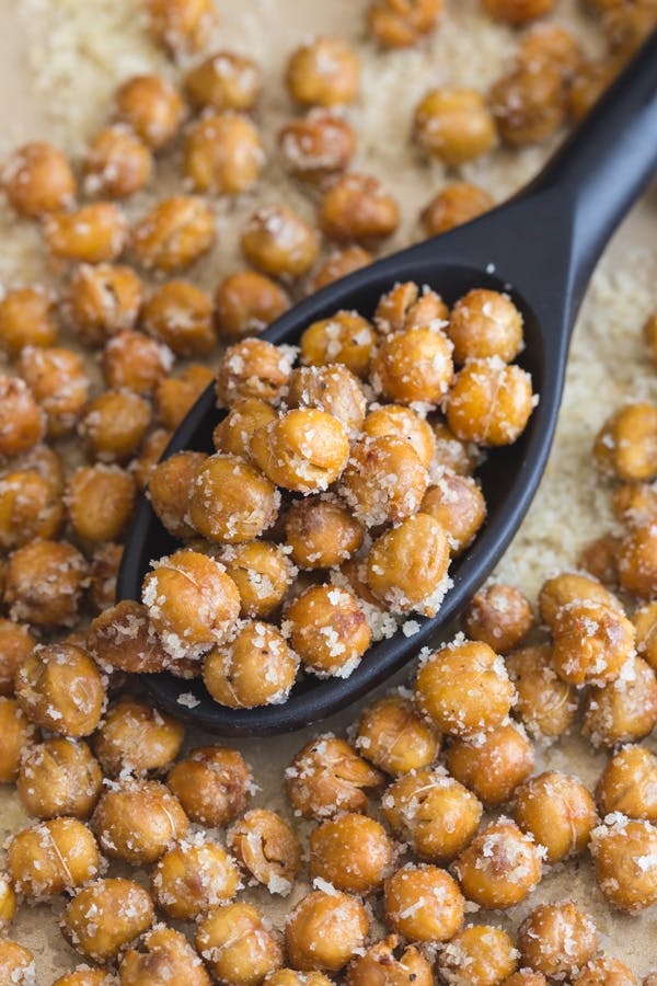 Roasted chickpeas on a black spoon and on parchment paper.