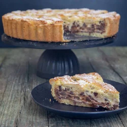 Romand ricotta crostata on a black cake plate with a slice on a black plate.