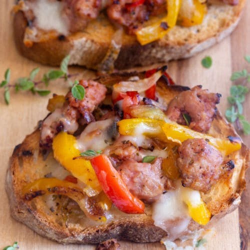 Bruschetta with sausage & peppers on a wooden board.