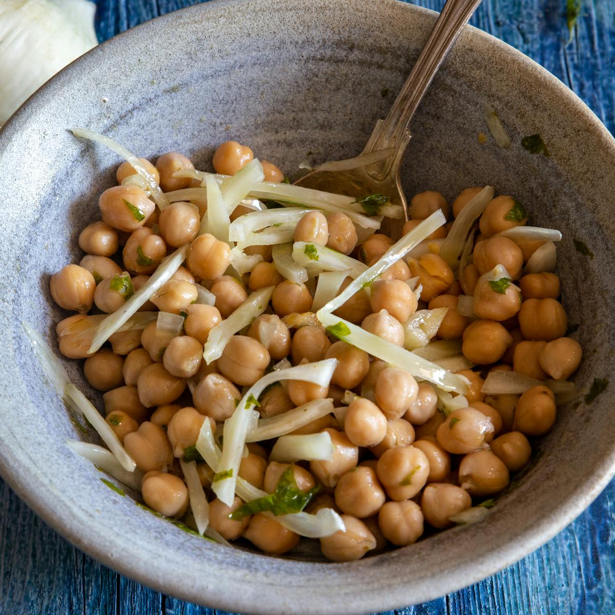 Chickpea salad in a blue bowl with a silver spoon.