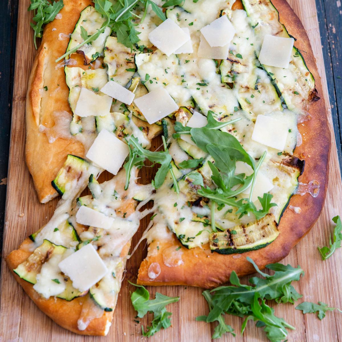 Zucchini pizza with a slice cut on a wooden board.