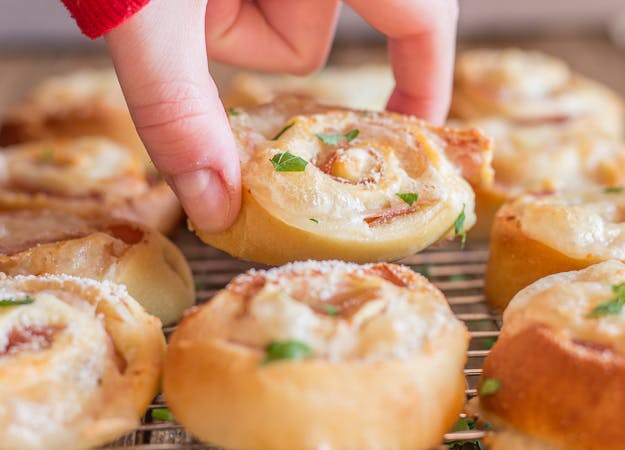 pizza rollups on wire rack with fingers picking up one.