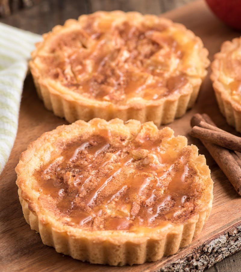 Caramel apple cheesecake tarts on a wooden board.