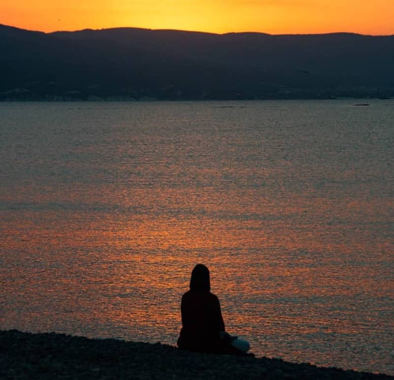 Silhouette of a person sitting by the ocean at sunset