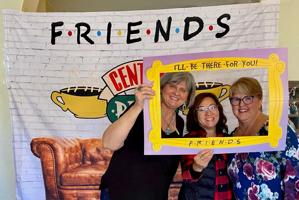 Susan Wahlers, Mindy Skelton (board member), and Stacey Kelley hold up a FRIENDS sign that says I'll be there for you in front of a FRIENDS bannnerr