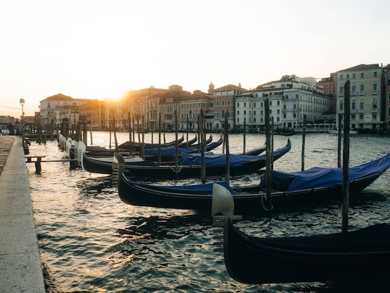 Gondolas docked along a canal in venice at sunset