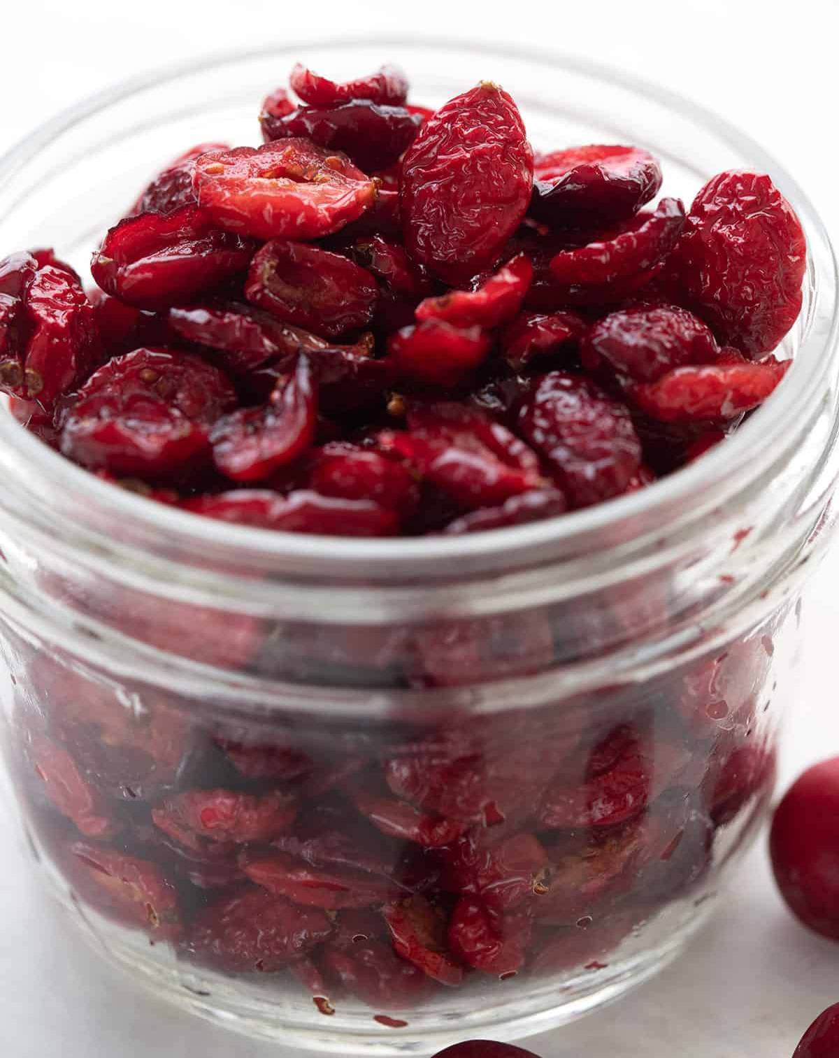 A jar of sugar free dried cranberries with fresh cranberries around it.