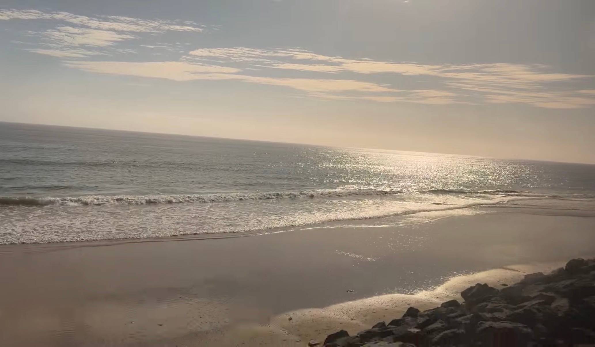 lapping ocean waves along a narrow shore, beneath a blue sky with some clouds