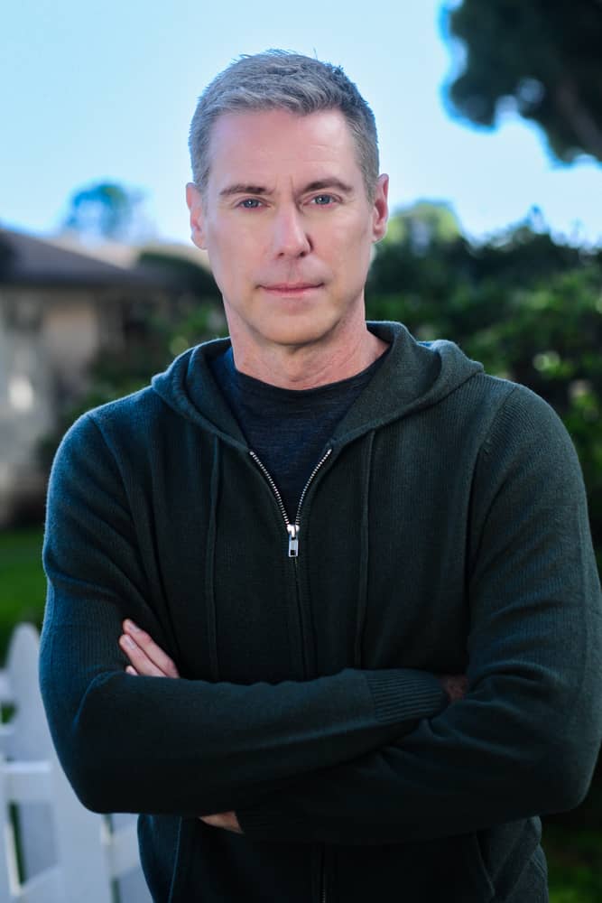 Wearing a dark red zippered pullover and a serious expression, Roy looks at the camera