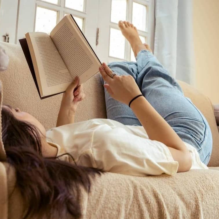 A woman laying on a couch reading a book