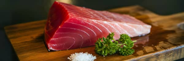 fresh raw tuna fish on a wooden plank with parsley and salt in front of it