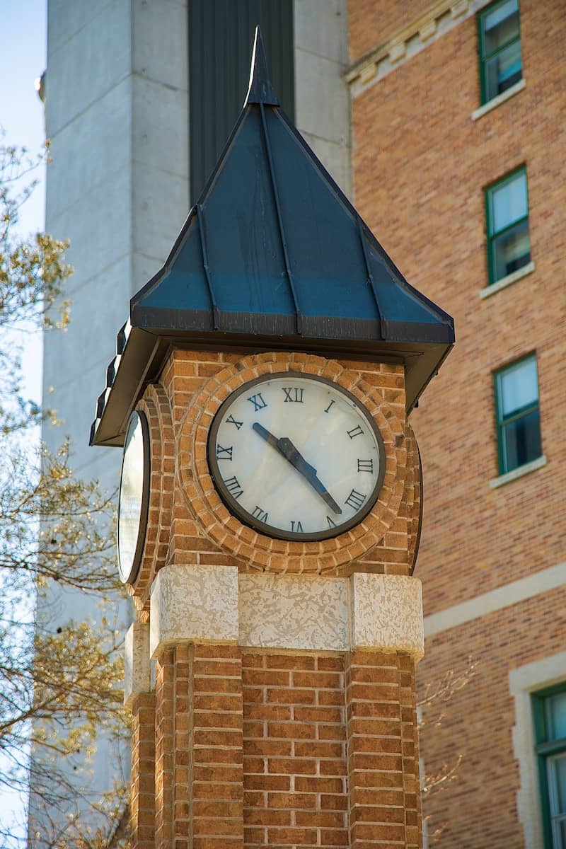 A brick clock tower stands against a brick building.