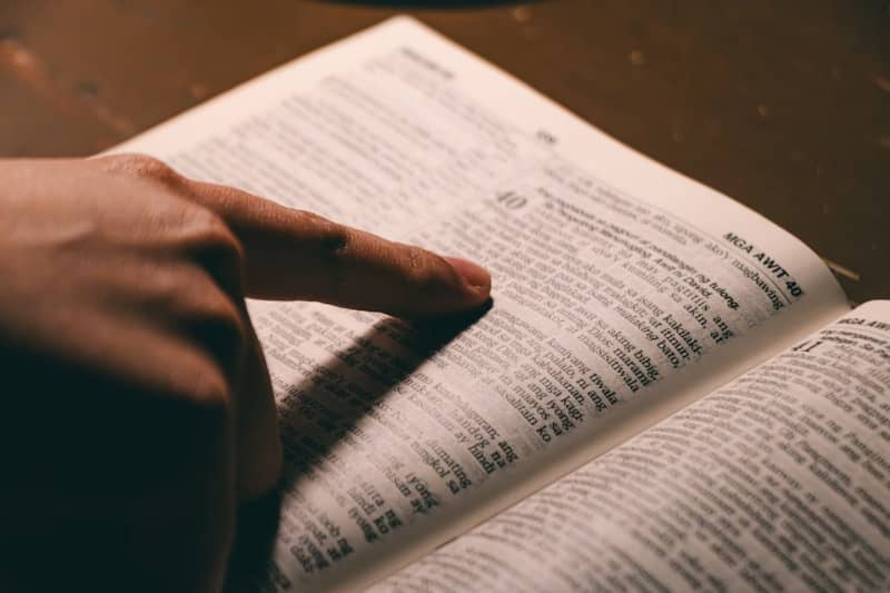 A finger points to a page in an open book.