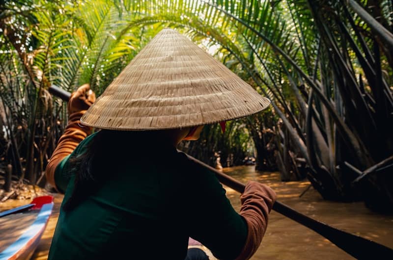 A person rows a boat in a lush canal.