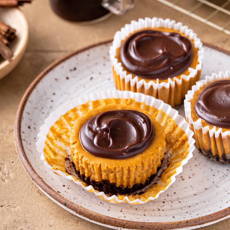 Three mini pumpkin cheesecakes on a plate. One of them is unwrapped.