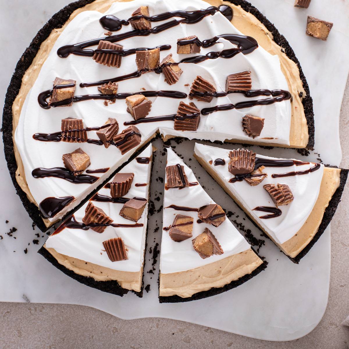 Overhead view of a sliced peanut butter pie topped with whipped cream, reese's cups and chocolate sauce.