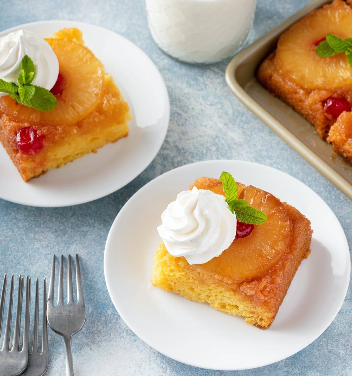 Two plates of pineapple upside-down cake, each topped with whipped cream.