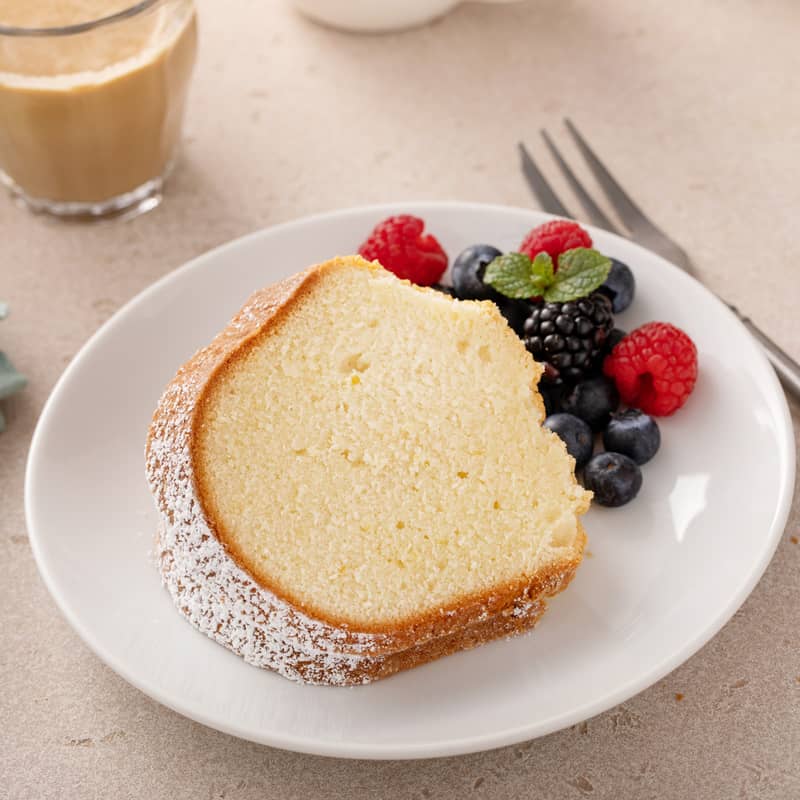 Slice of cream cheese pound cake on a white plate next to mixed fresh berries.