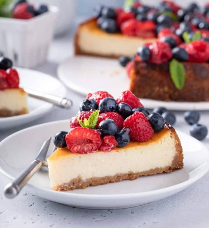 Slice of ricotta cheesecake topped with red and blue berries, set on a white plate.