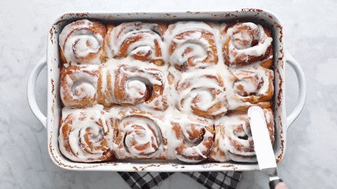 Gif of spreading frosting over TikTok cinnamon rolls in a white baking dish.