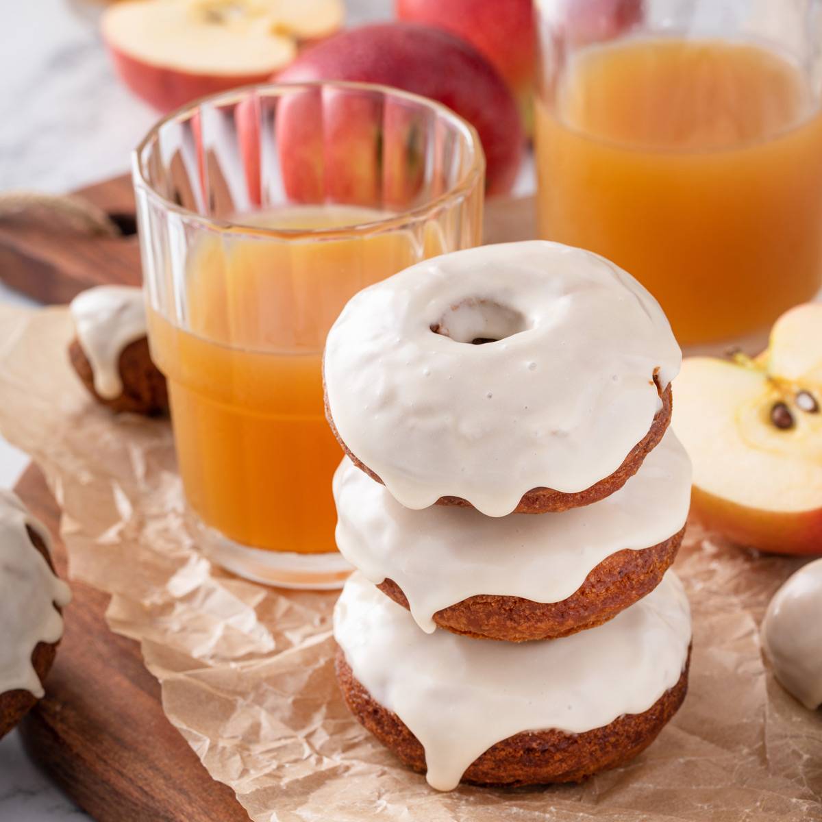 Three glazed apple cider donuts stacked next to a glass of apple cider.