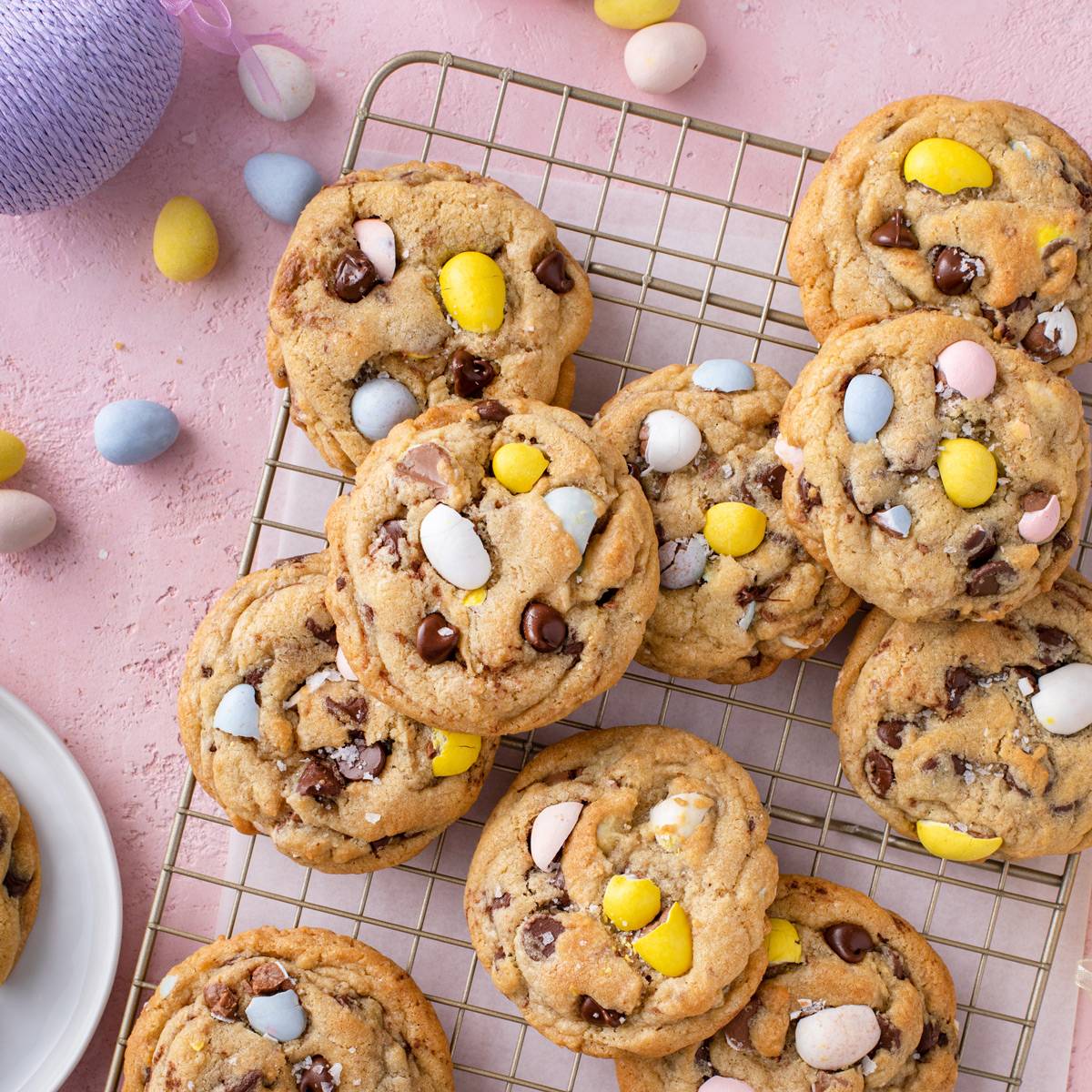 Cadbury egg cookies cooling on a wire rack over a pink countertop.