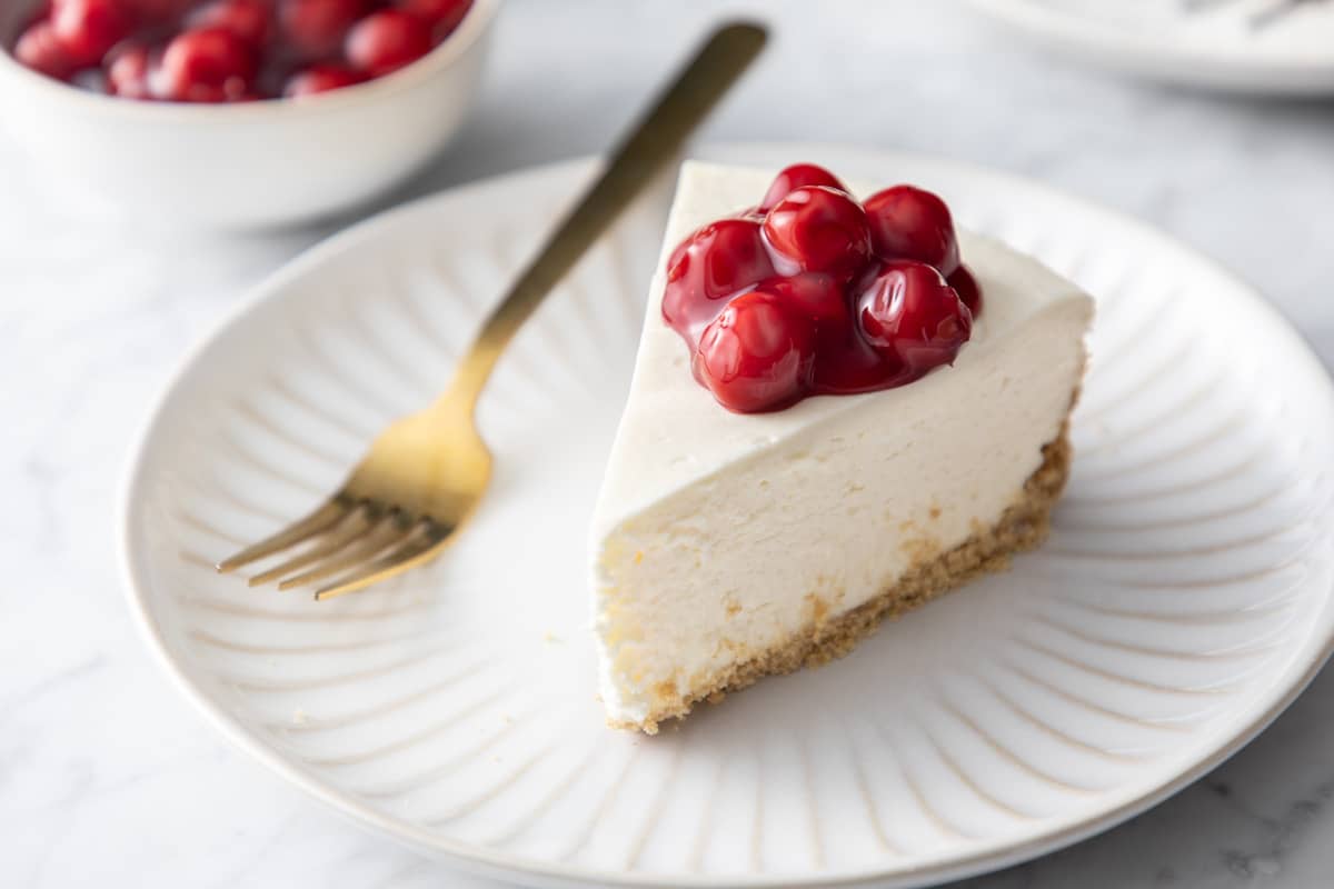 Slice of no-bake cheesecake, topped with cherry pie filling, on a white plate.