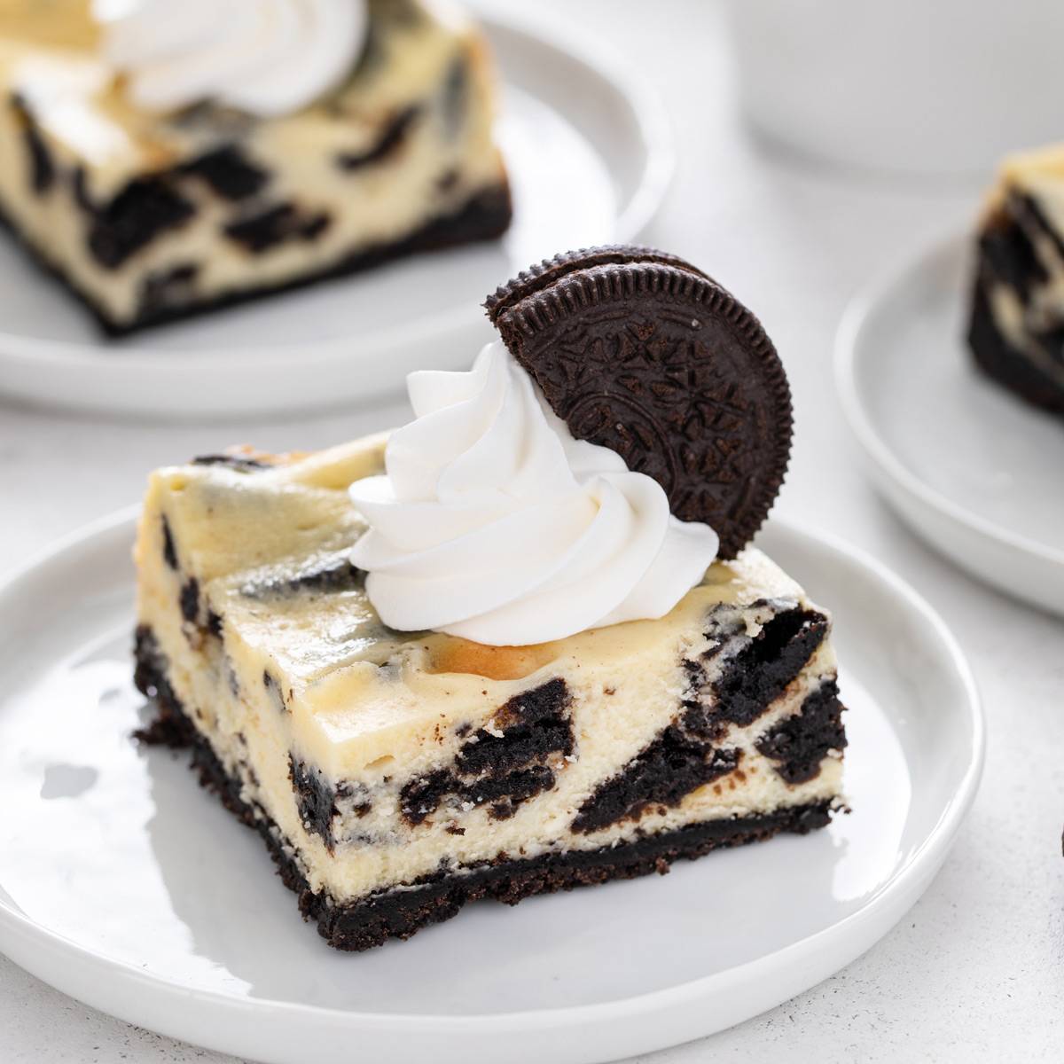 Oreo cheesecake bar garnished with whipped cream and an oreo on a white plate.