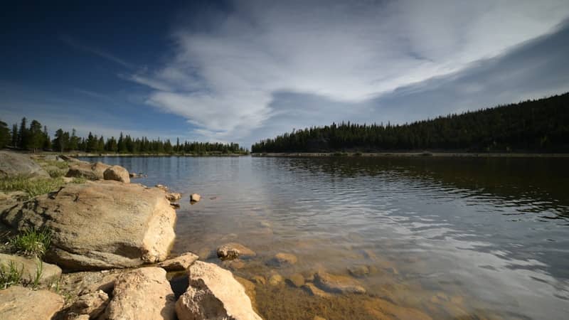 Rocky lake shore under a blue sky with white clouds.