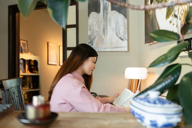 A woman reads a book by a lamp.