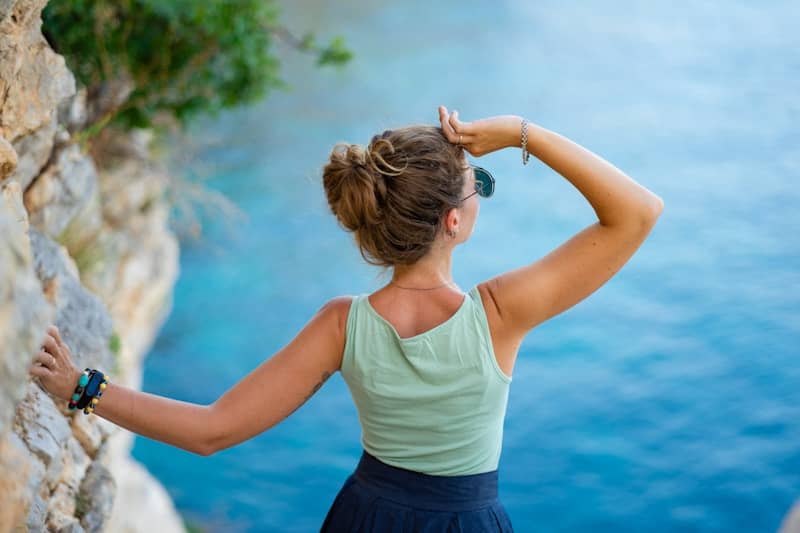 Woman looking out at the blue ocean from a cliff.
