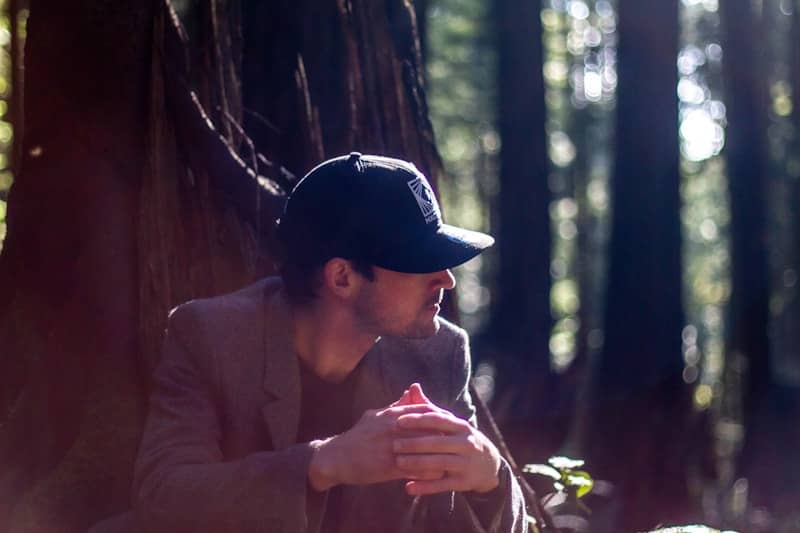 A man wearing a cap sits in a sunlit forest.