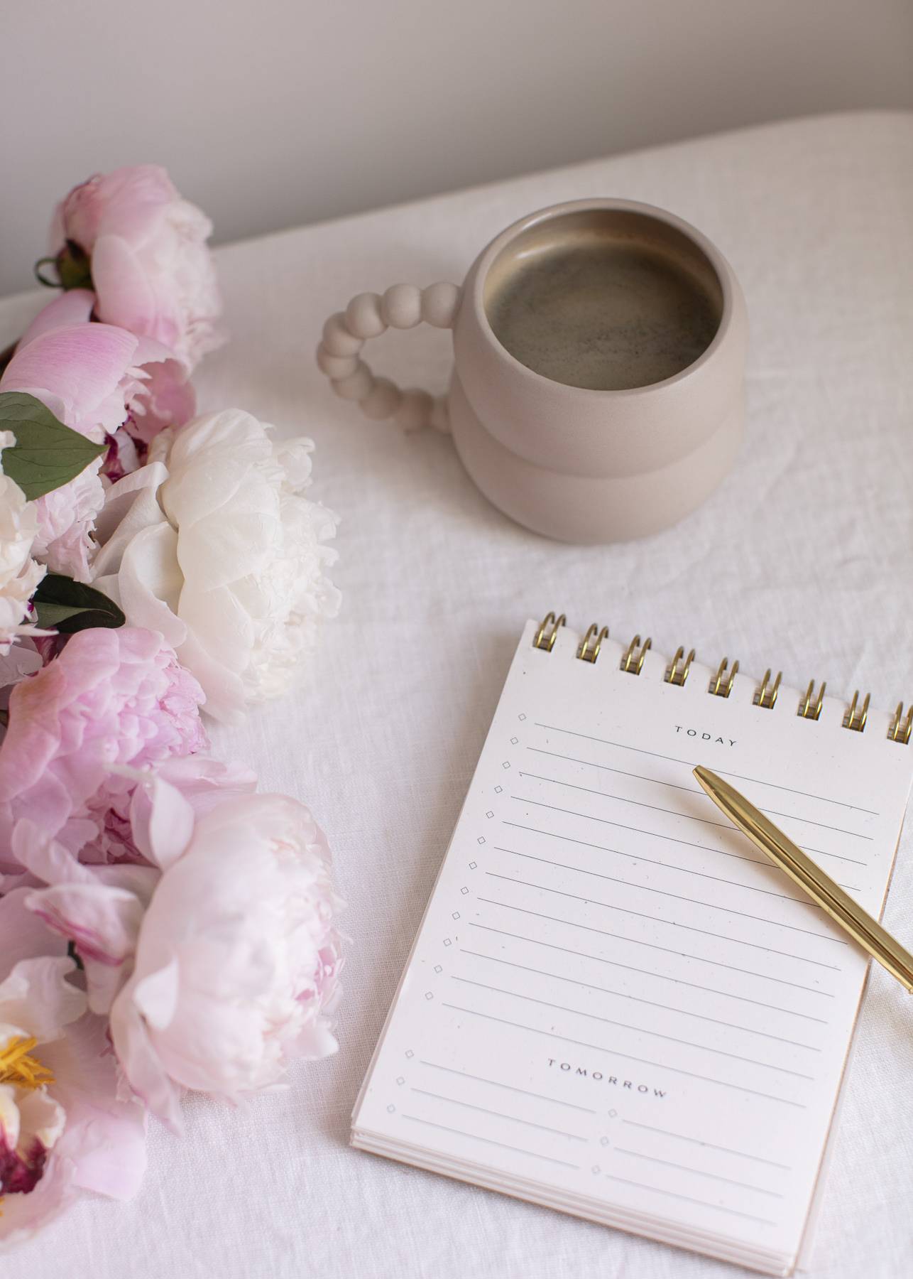 a notebook, pen, mug and flowers on a table 