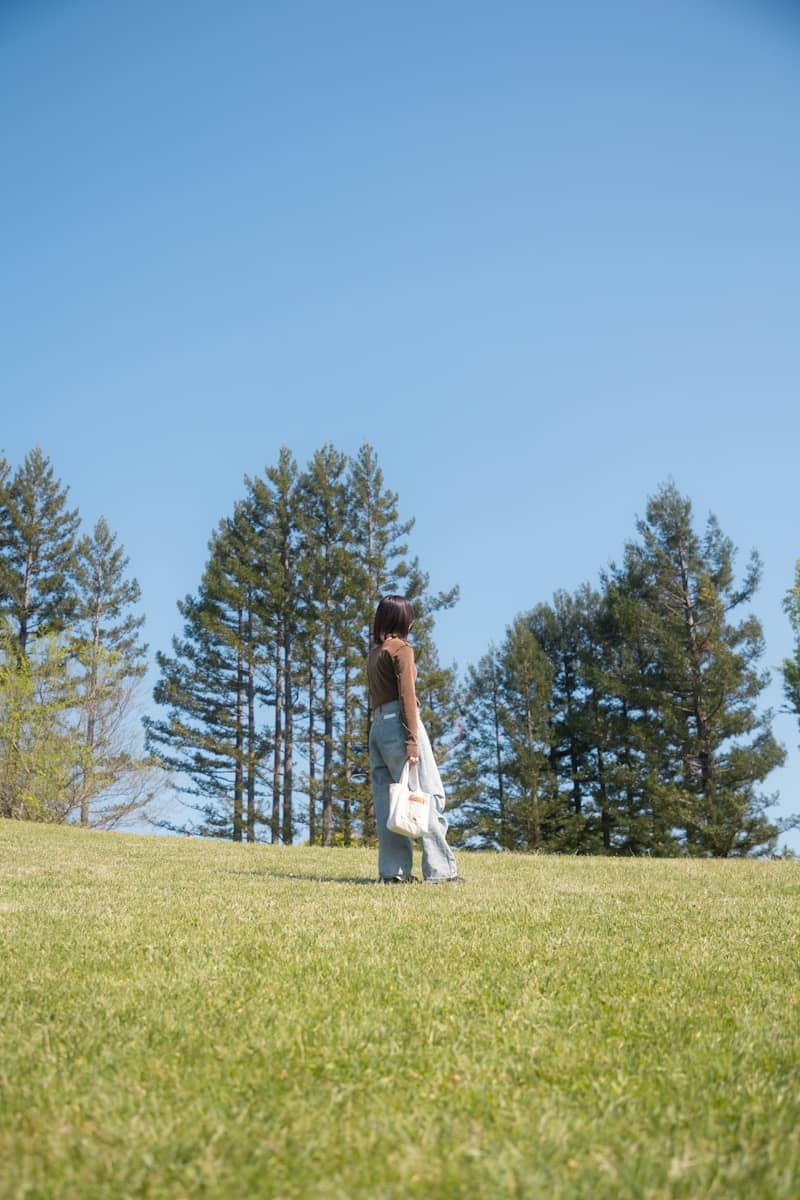 Woman stands on a grassy hill under a bright sky.
