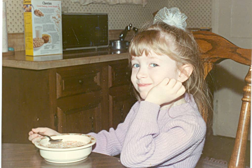 a little girl smiling with spoon and cereal bowl