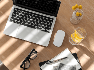 Flatlay of a laptop, planner, pen, and glasses on a sunlit desk—perfect workspace for introverted entrepreneurs focused on aligned business growth.