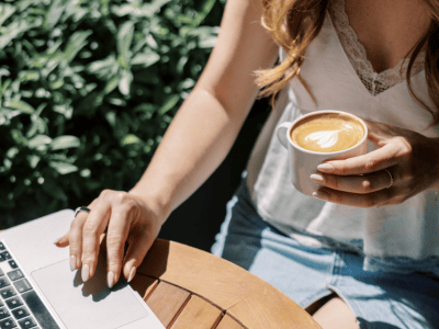 Woman holding coffee while working on laptop outdoors — calm workspace setup for protecting your energy and starting fresh in business at 50.