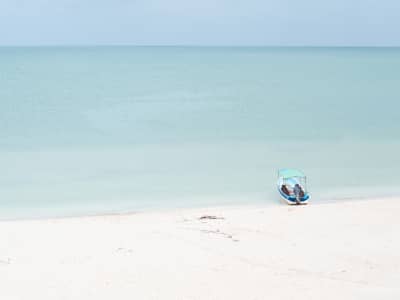 Small boat on calm turquoise water beside an empty beach—symbolizing quiet focus, sustainable business, and setting summer hours with intention.