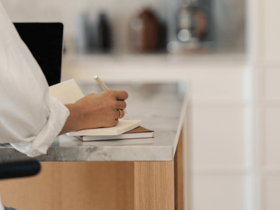 Person writing in a notebook at a clean desk, symbolizing business clarity and offer evaluation. Perfect for digital product strategy reflection.